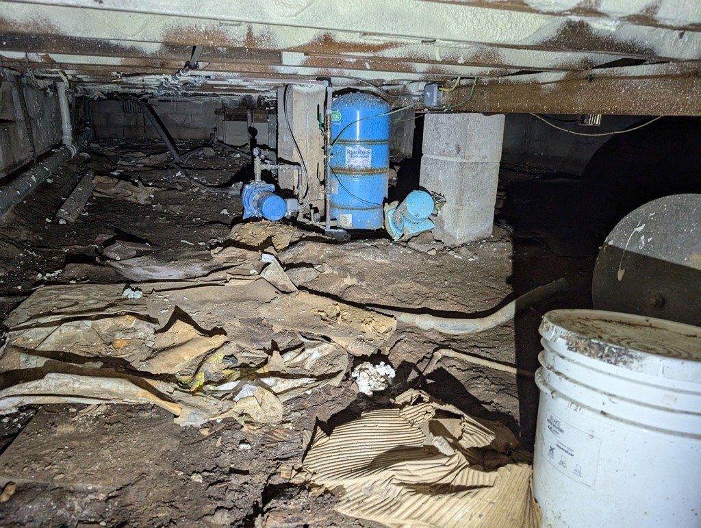 Dirty and damp crawl space with exposed pipes, debris, and moisture issues before encapsulation