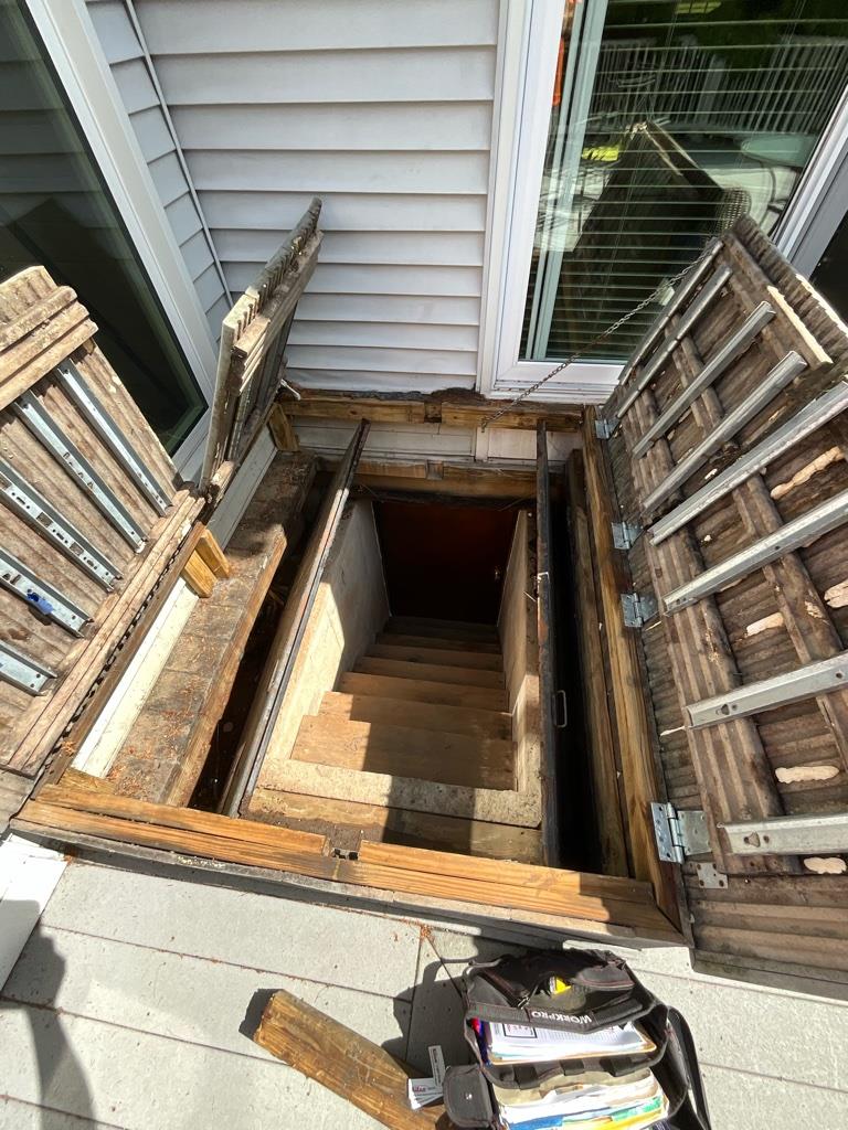 Old Bilco door under deck in Cheshire, CT showing improper installation and poor drainage around basement stairwell
